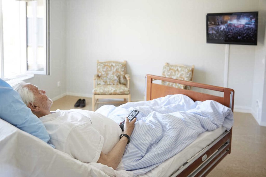 Senior man watching TV while reclining on bed in hospital ward