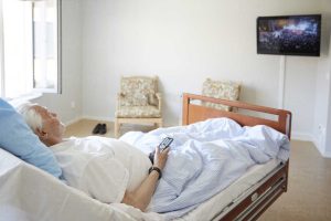 Senior man watching TV while reclining on bed in hospital ward