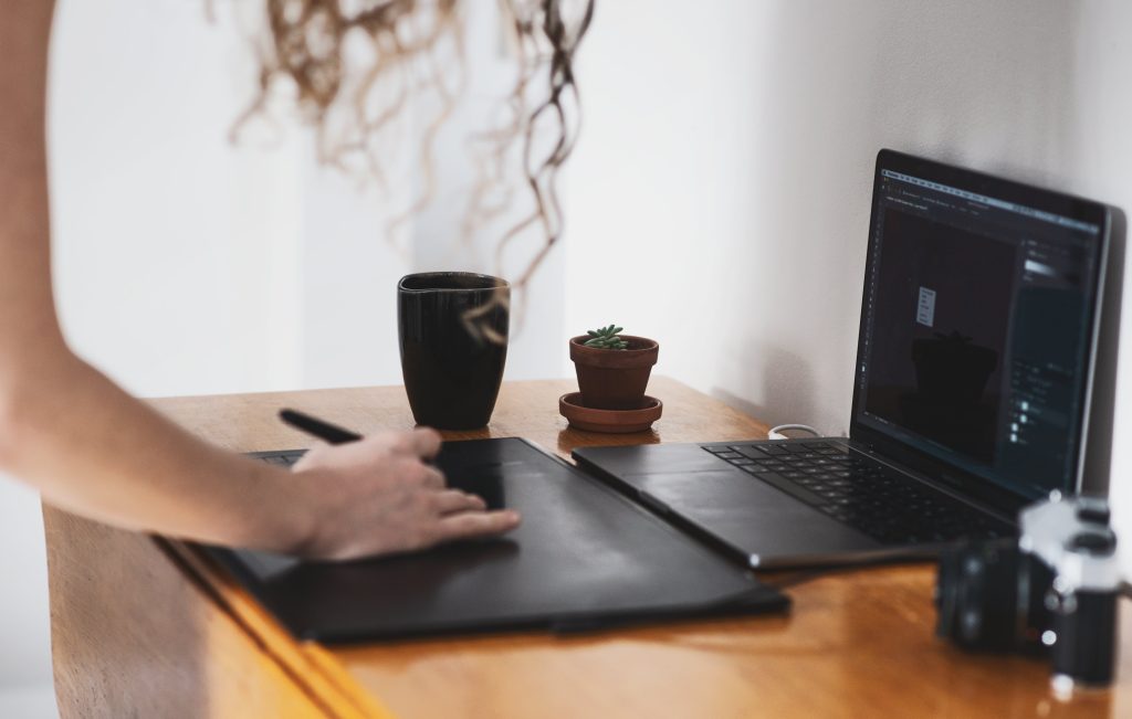 person-leans-over-to-use-a-pen-tablet-in-front-of-a-laptop